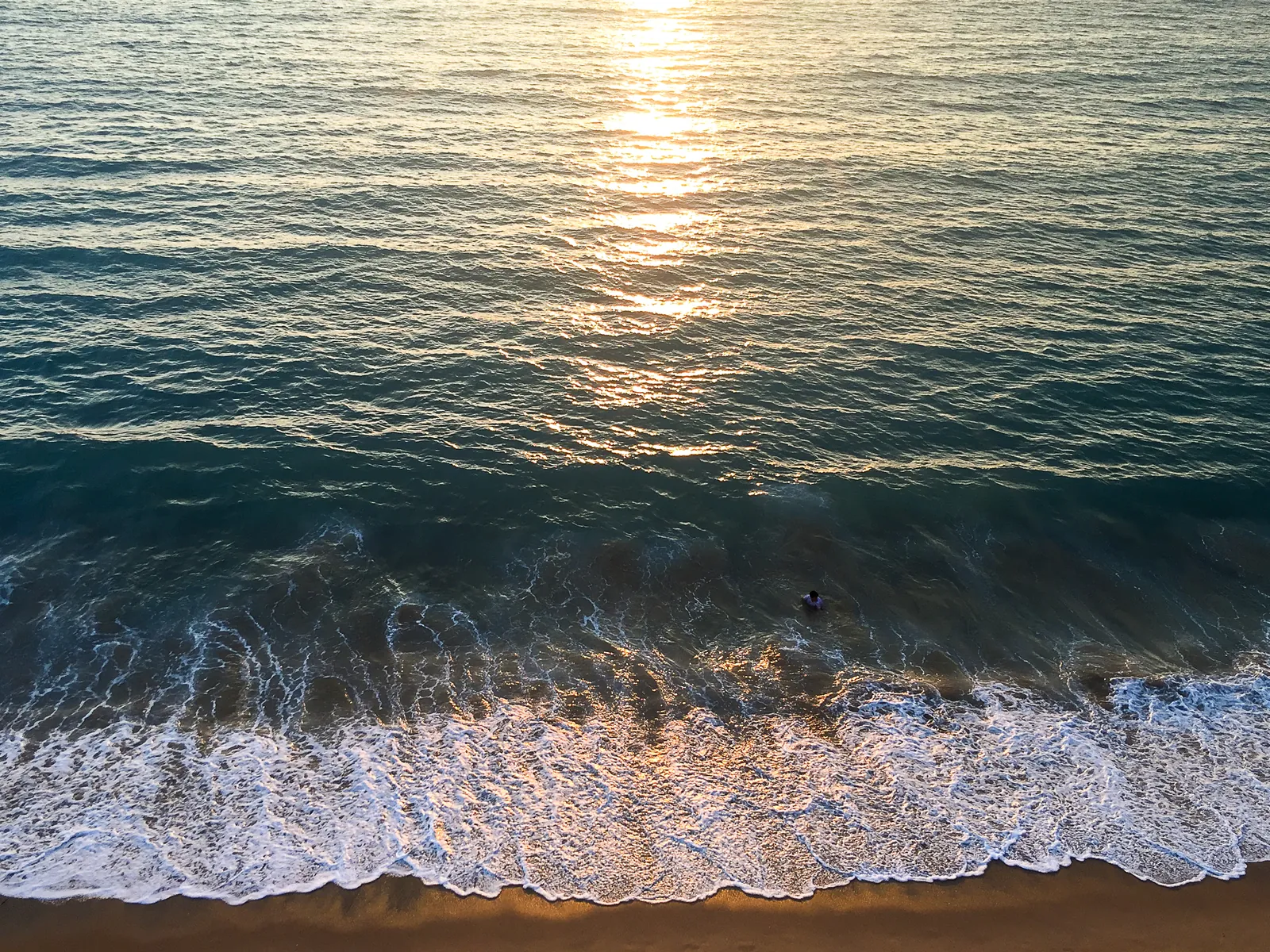 Vista aérea del atardecer sobre la playa, con una persona sola en el agua