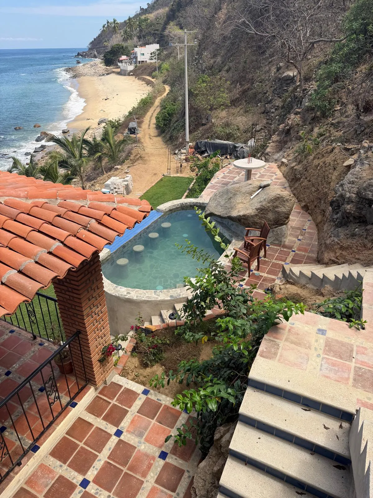 Vista desde arriba de la alberca de piedra de Villa Chimo, el techo de teja y la playa de Chimo al fondo