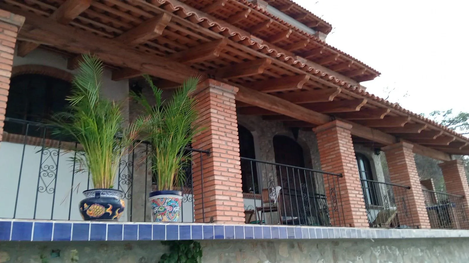 Fachada de Villa Chimo con pergolado de madera, teja y macetas de talavera