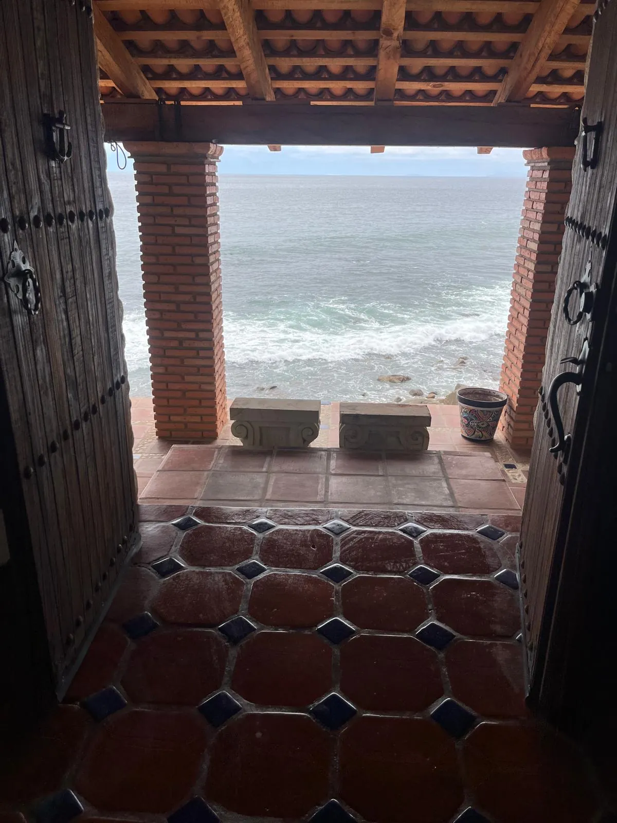 Puerta principal de madera abierta directo al mar, con piso de barro y talavera